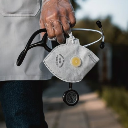 medical professional in white lab coat holding stethoscope and face mask