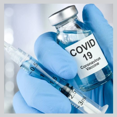 gloved hand with syringe and bottle of covid 19 vaccine